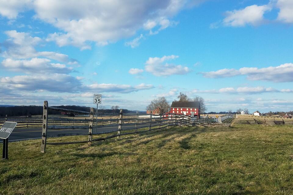 Paisatge rural amb un senyal de límit de velocitat, una granja vermella i una tanca de fusta.