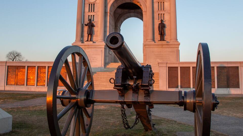 A cannon in front of a monument with inscriptions and statues.