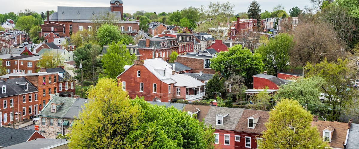 A town with red brick buildings, a church with a steeple, and green trees.