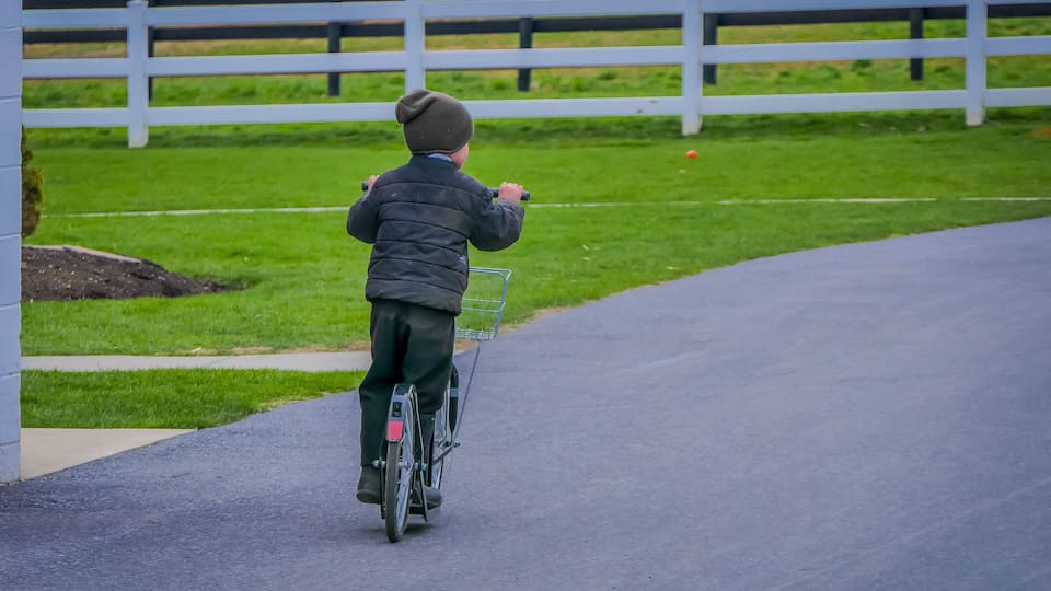 A child riding a bicycle on a paved path with a white fence in the background.