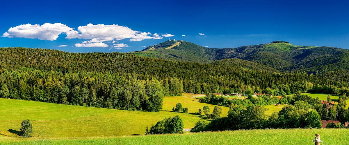 A mountainous landscape with a village nestled among green fields and dense forests.