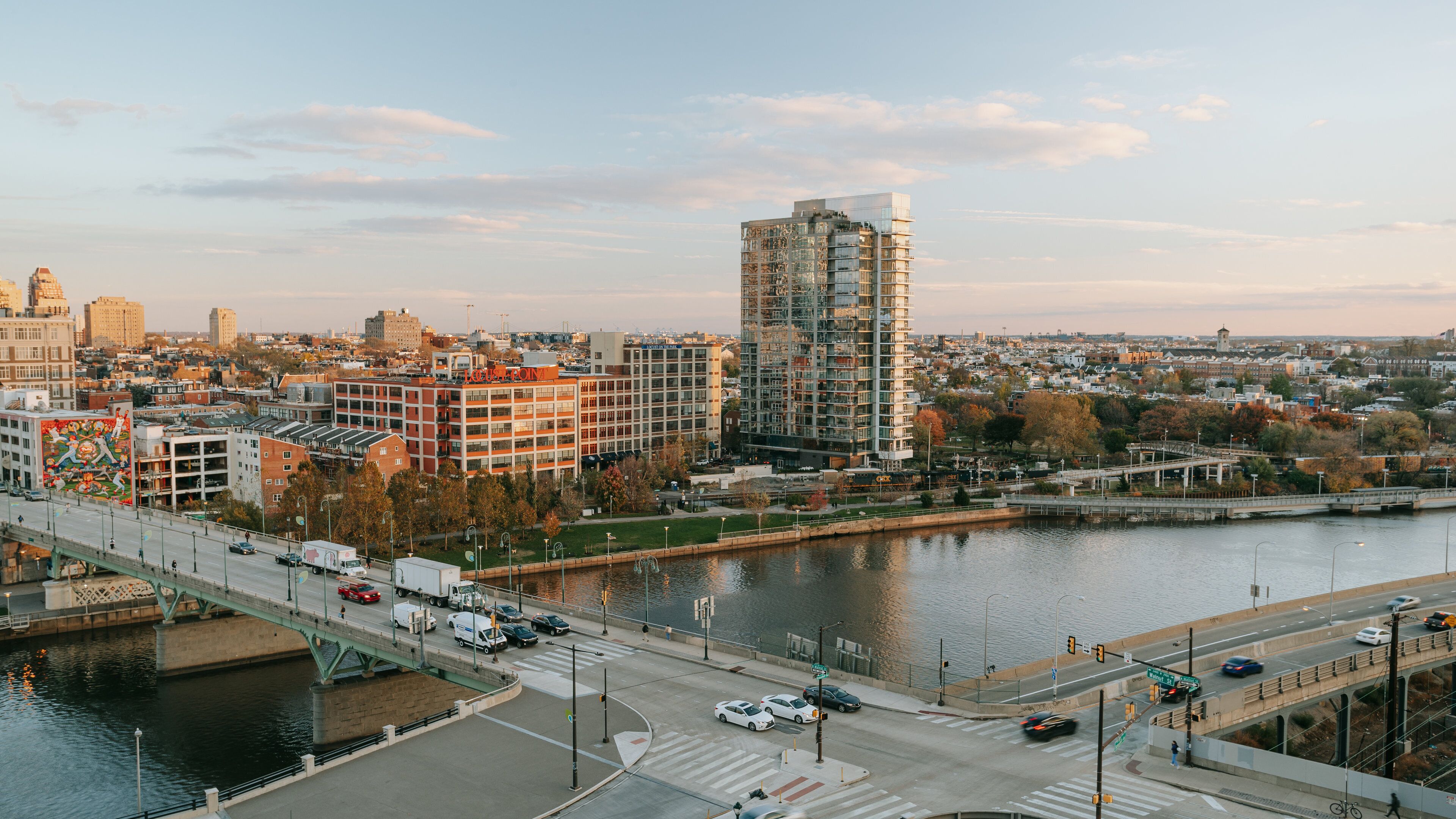 A cityscape with a river, a bridge, and various buildings including a tall, modern structure.
