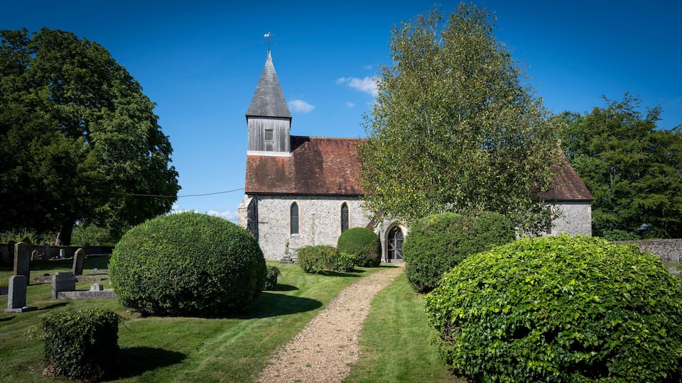 A church with a steeple, surrounded by well-maintained hedges and a gravel path.