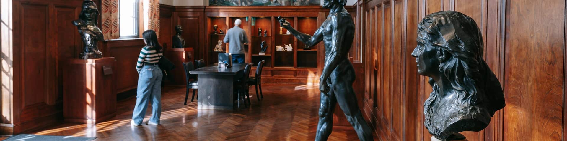 A museum interior with wooden paneling, a large painting on the wall, and bronze sculptures.