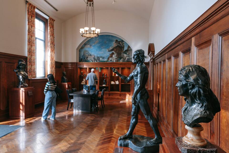 A museum interior with wooden paneling, a large painting on the wall, and bronze sculptures.
