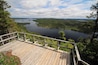 A wooden viewing platform overlooking a lake surrounded by dense forest and distant hills.