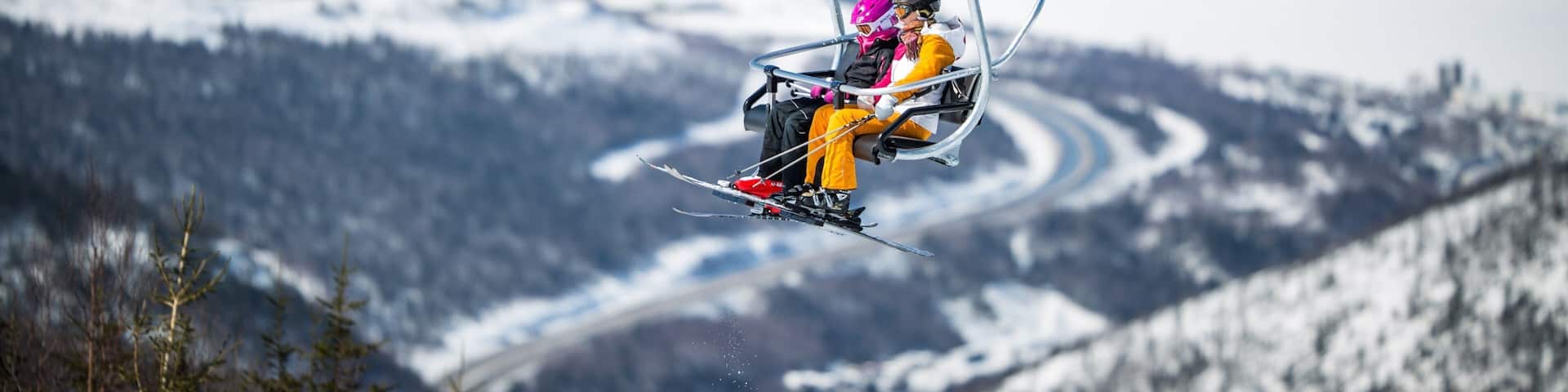A ski lift chair with two skiers in a snowy mountainous landscape.