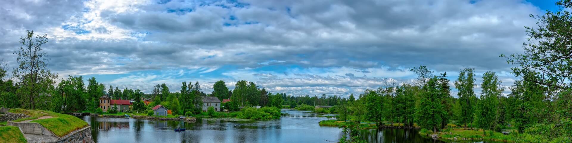 Panorama of the banks of sleepy Vuoksa River at sunny summer day. Priozersk, Russia.