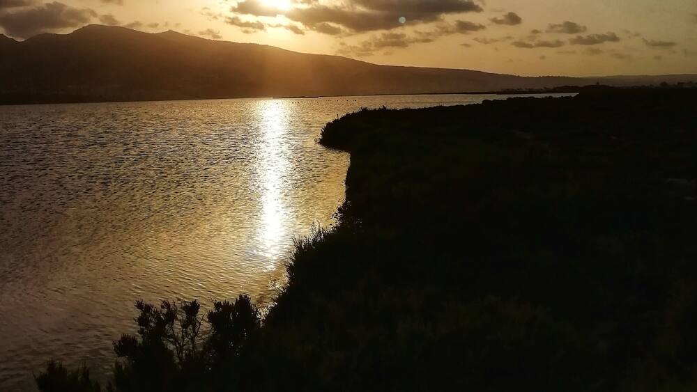 Ein Sonnenuntergang über einem ruhigen See mit der Silhouette eines entfernten Gebirges.