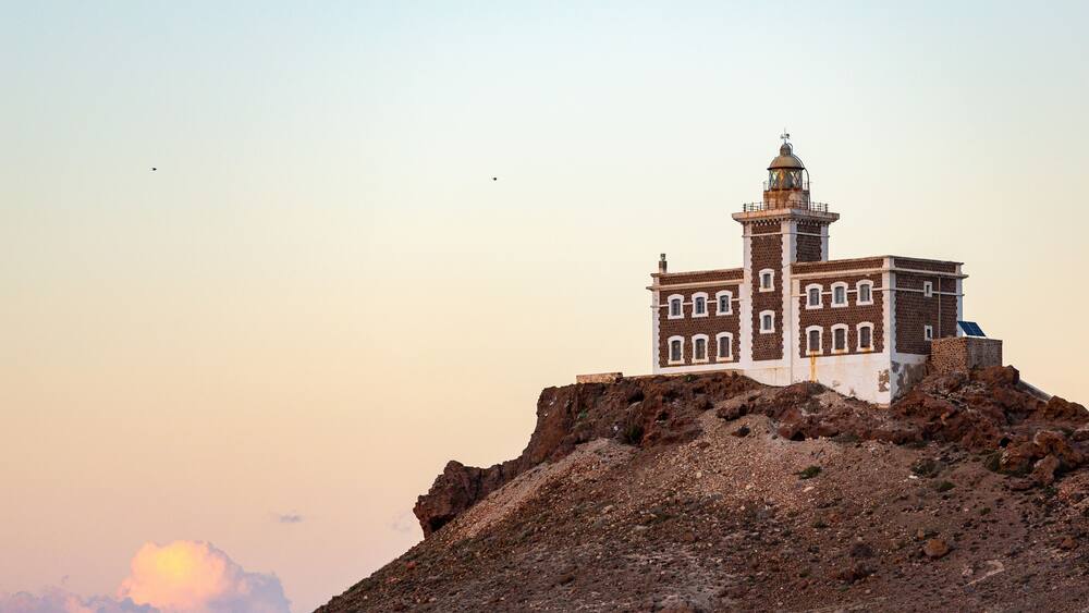 Un phare perché sur une colline rocheuse, sous un ciel dégagé.