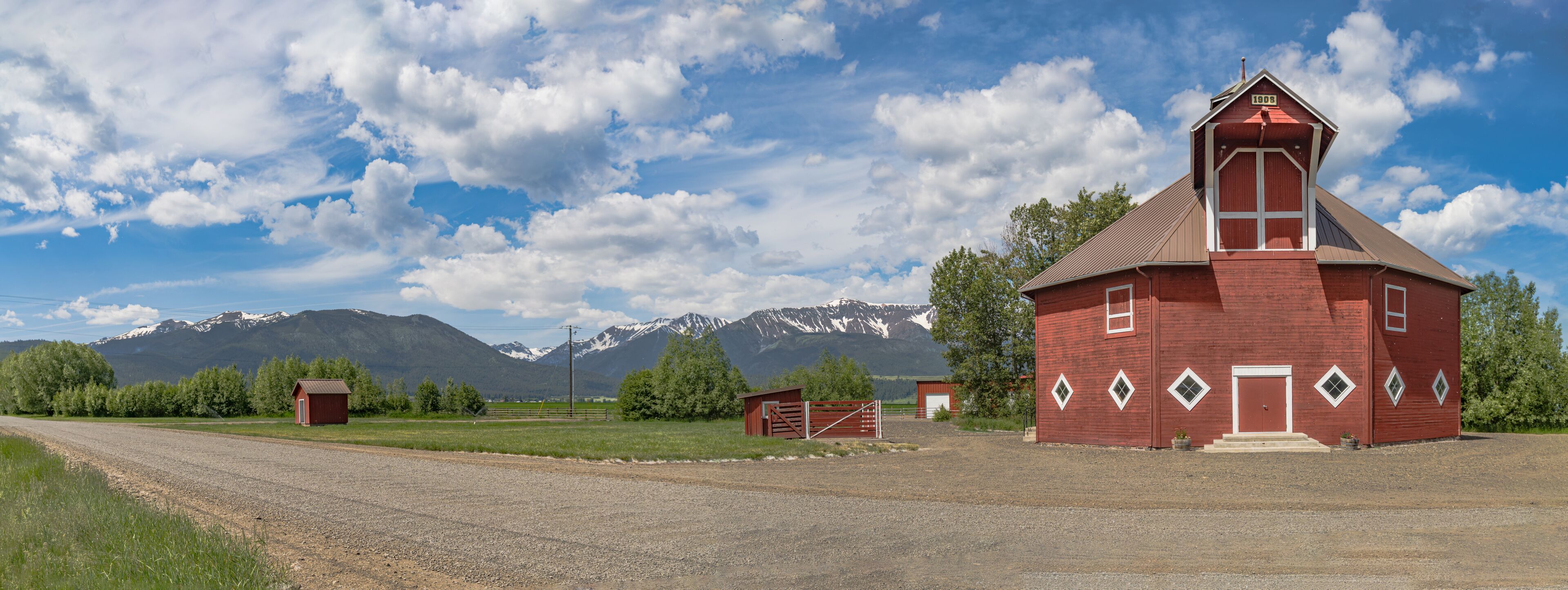 A red barn with a white door, a gravel road, and snow-capped mountains in the background.