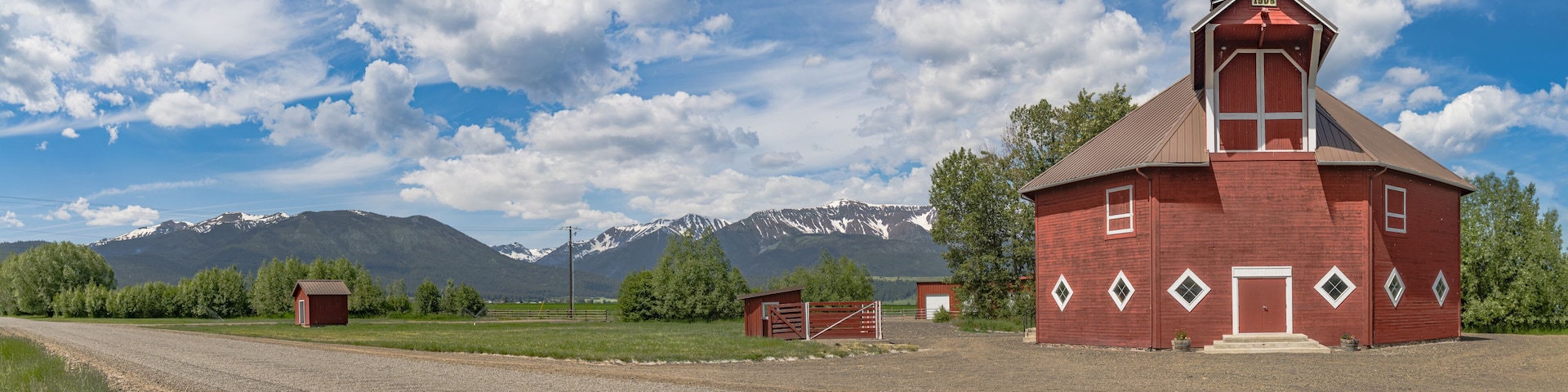 A red barn with a white door, a gravel road, and snow-capped mountains in the background.