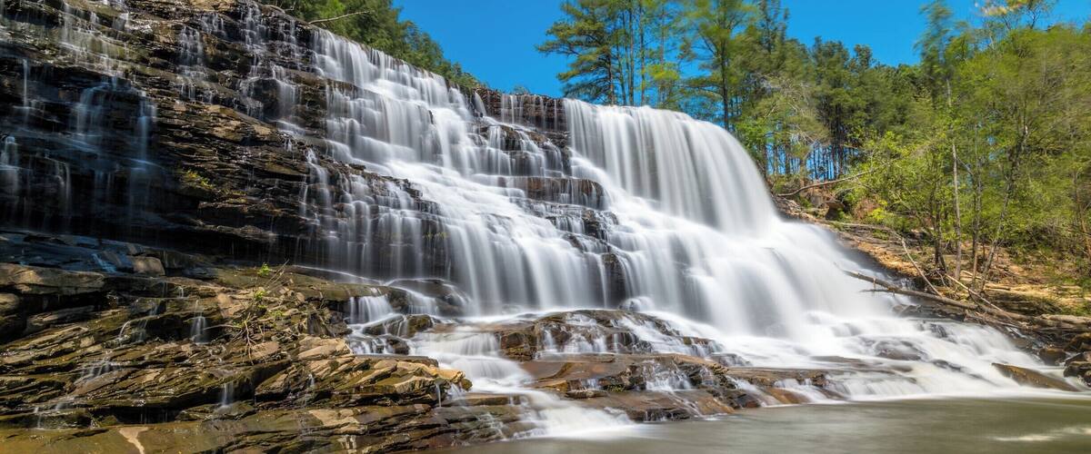 A multi-tiered waterfall surrounded by dense forest.
