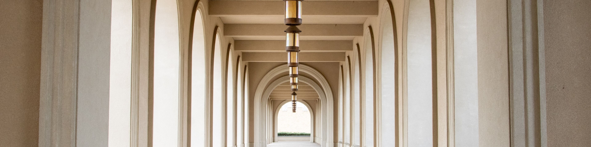Um corredor longo com arcos e um candeeiro pendente.