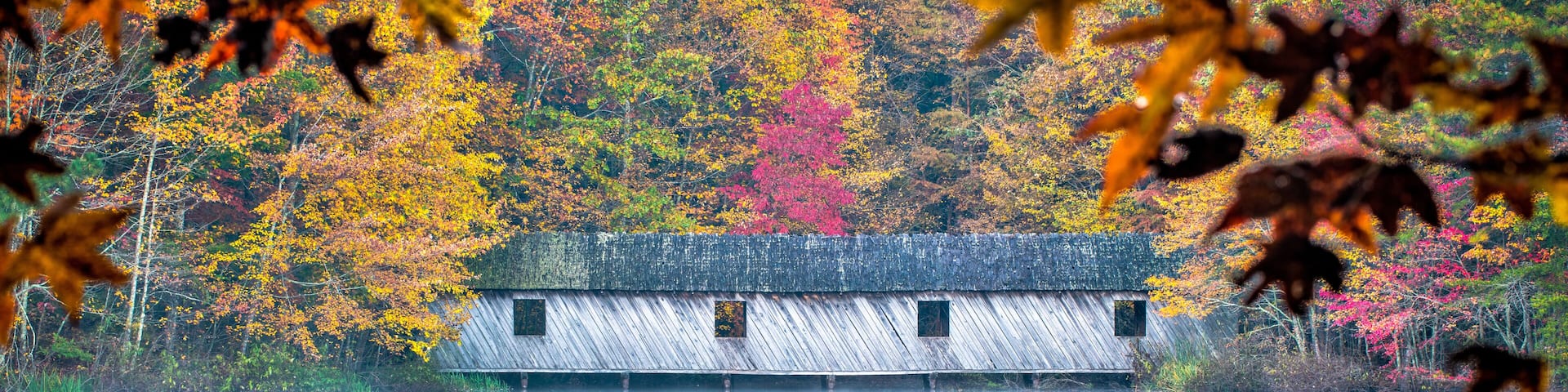Covered bridge in the fall, As mist rises from the calm waters, fall colors are reflected around the covered bridge.