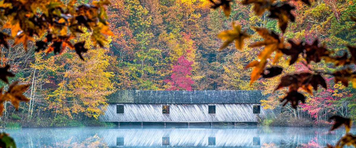 Covered bridge in the fall, As mist rises from the calm waters, fall colors are reflected around the covered bridge.