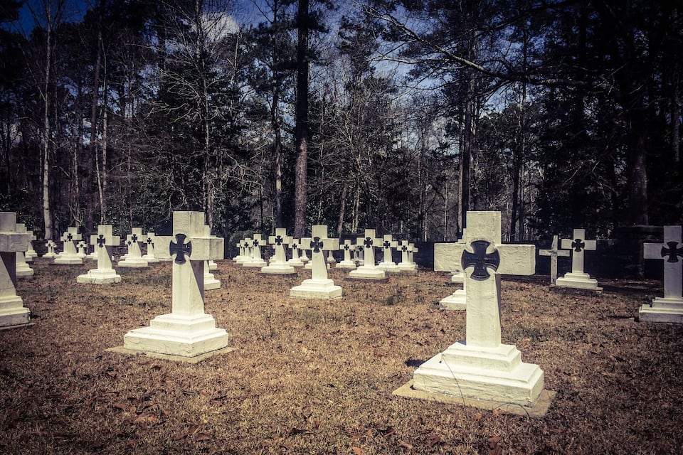 A cemetery with numerous white crosses and tombstones, surrounded by trees.