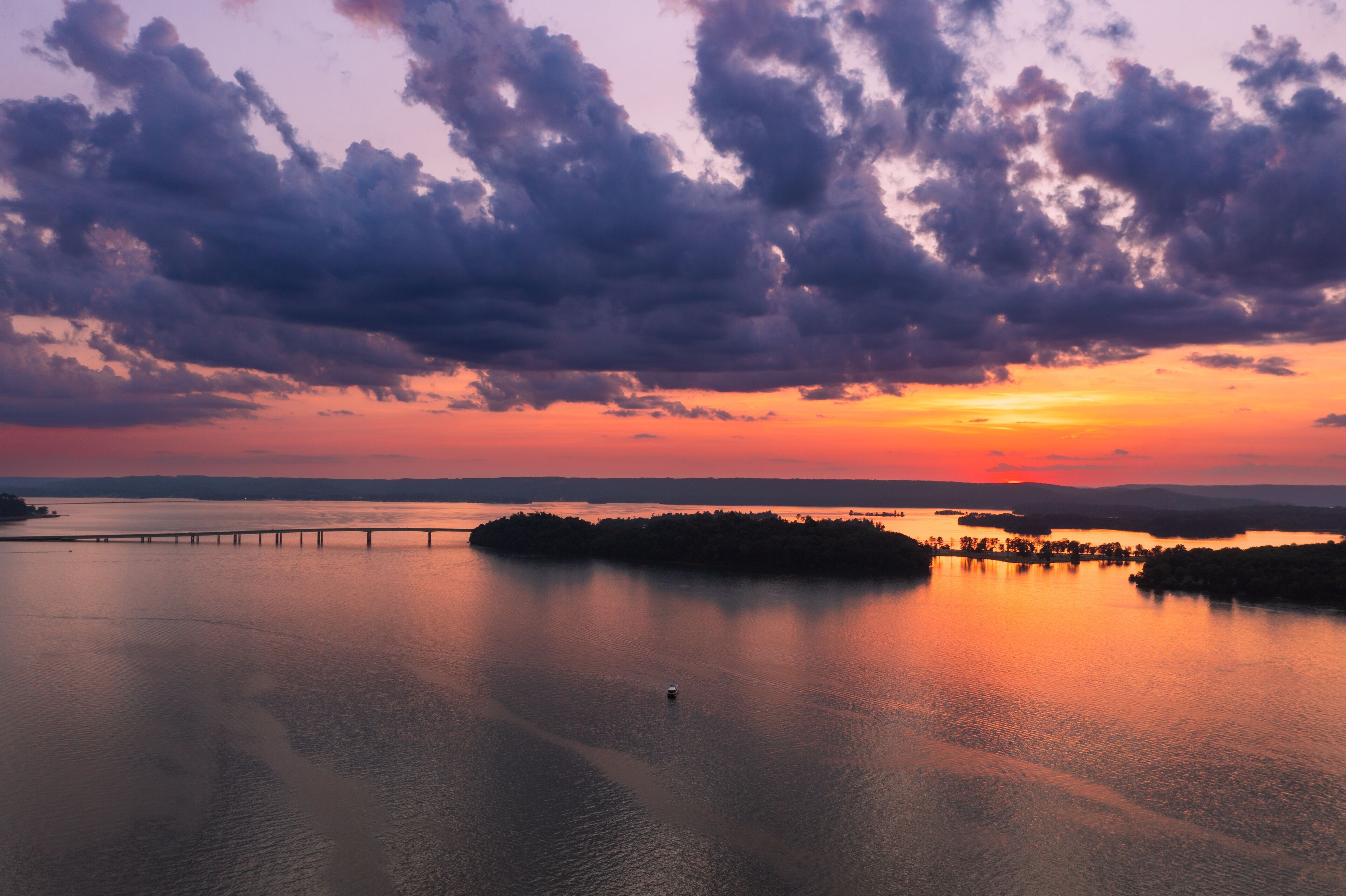 A sunset over a calm body of water with a bridge and an island.