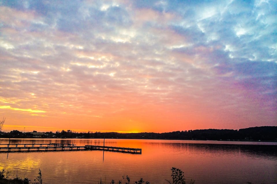 A sunset over a calm lake with a dock extending into the water.