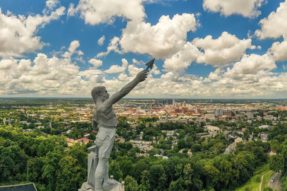 Una estatua de un hombre sosteniendo una cometa, con vistas a un paisaje urbano con edificios y áreas verdes.