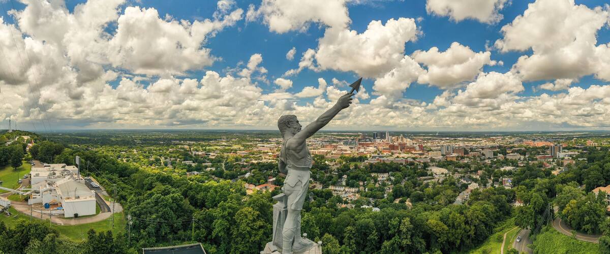 A statue of a man holding a kite, overlooking a cityscape with buildings and greenery.