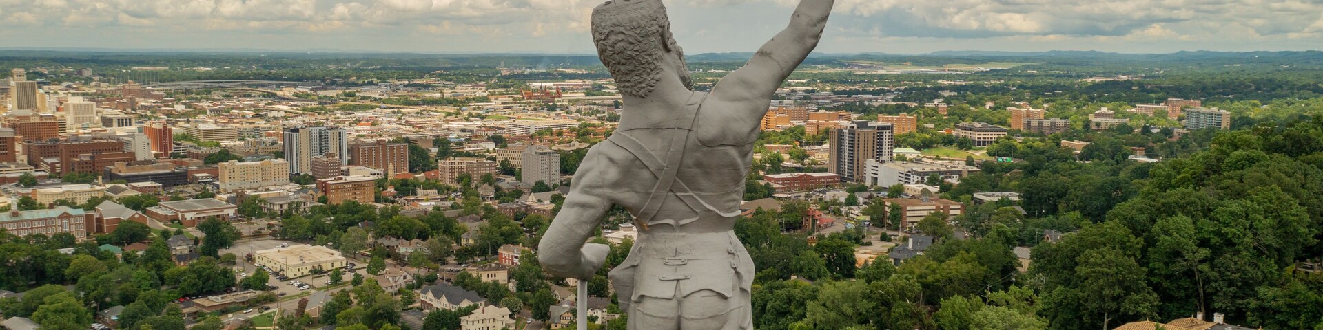 Uma estátua com vista para um horizonte urbano repleto de edifícios e áreas verdes.