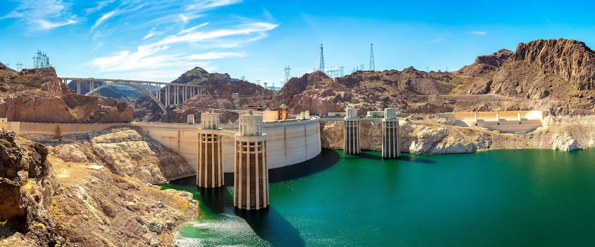 A hydroelectric dam with a bridge, rocky terrain, and a reservoir.