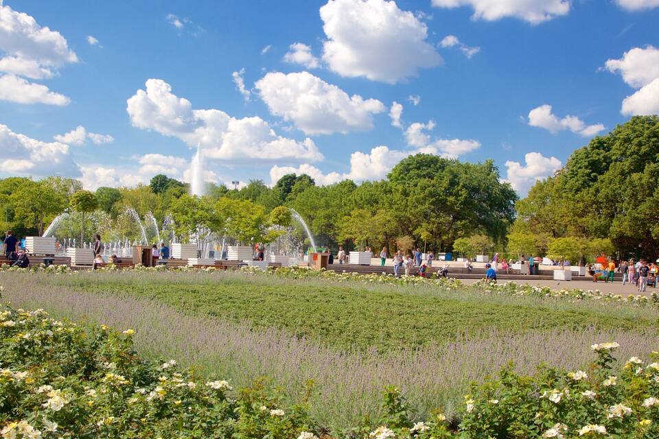 A park with a fountain, flower beds, and people walking.