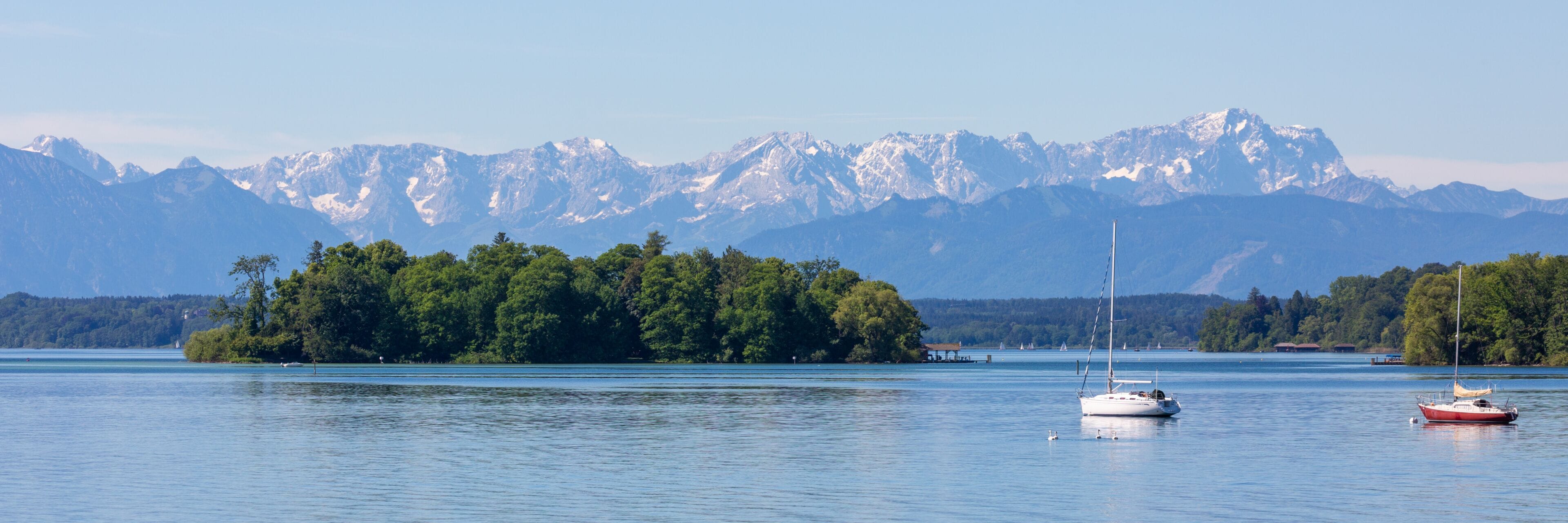 Panorama of Lake Starnberg with Roseninsel, alps and sailboats. Popular travel destination.