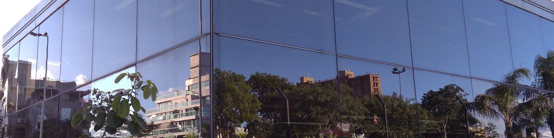 Um edifício moderno de vidro refletindo árvores e edifícios ao redor.