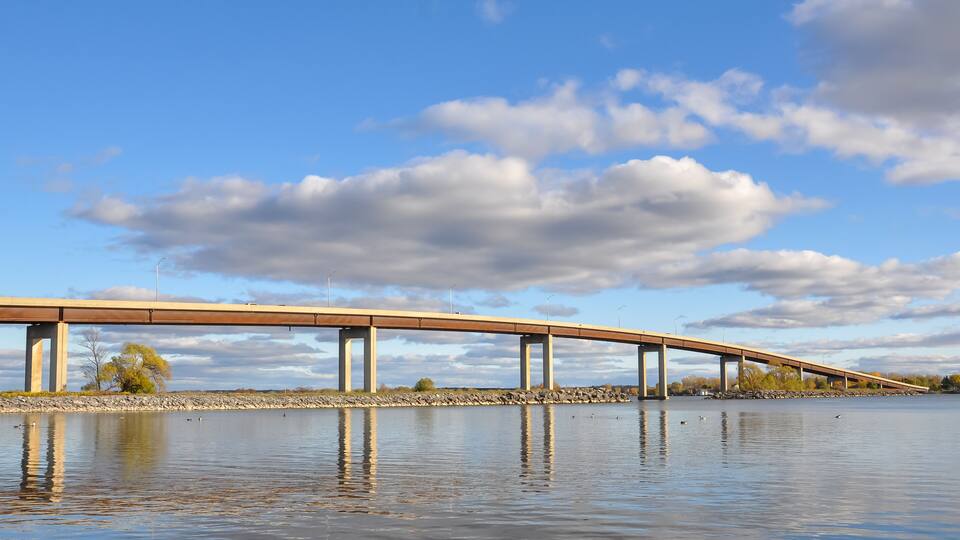 A bridge over a calm body of water with a clear sky and some clouds.