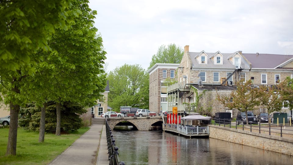 A canal with a stone bridge, a row of parked cars, and buildings with stone facades.