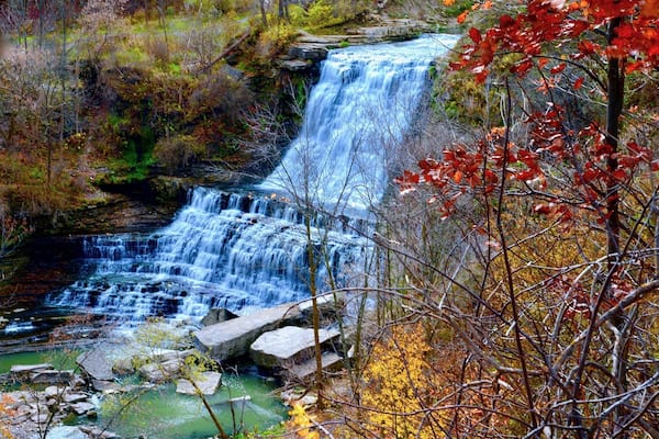 A waterfall cascading over rocks in a forested area with autumn foliage.