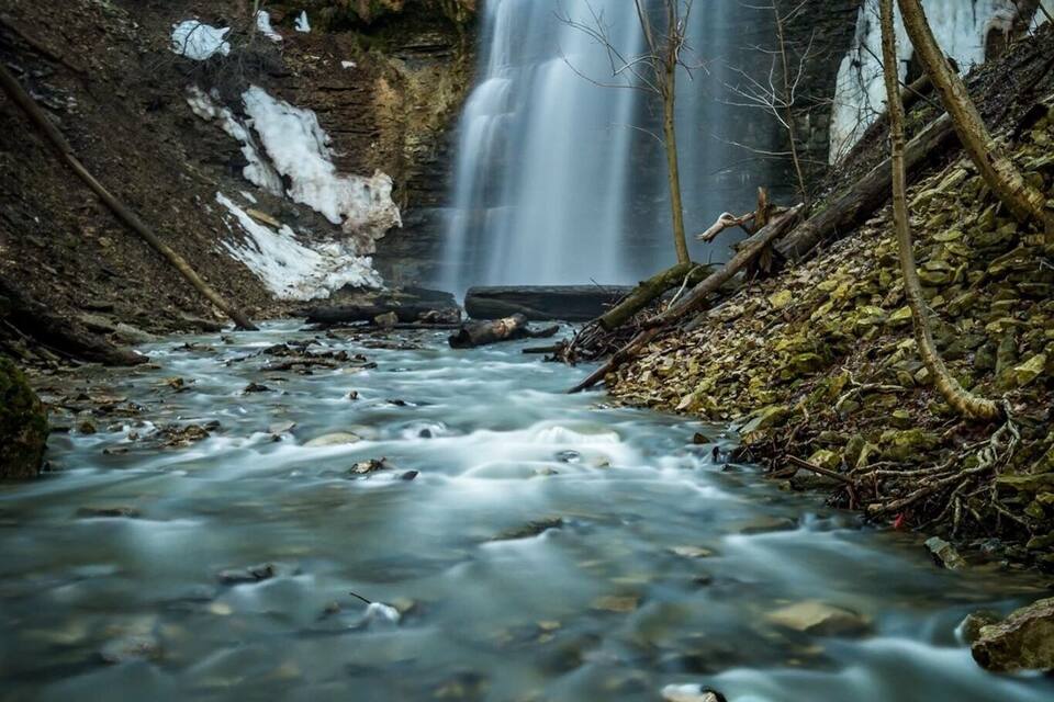 A waterfall cascading into a clear stream surrounded by rocky terrain and sparse vegetation.