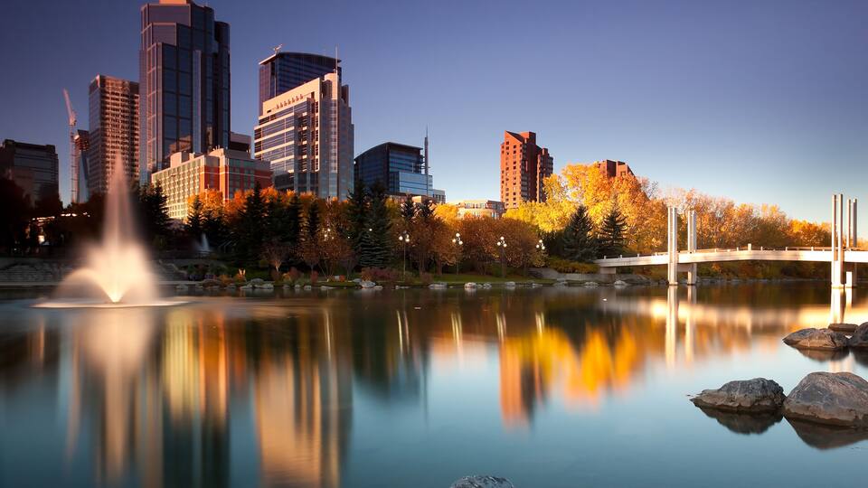 Un horizonte urbano con edificios modernos, un lago tranquilo, árboles otoñales y un puente.