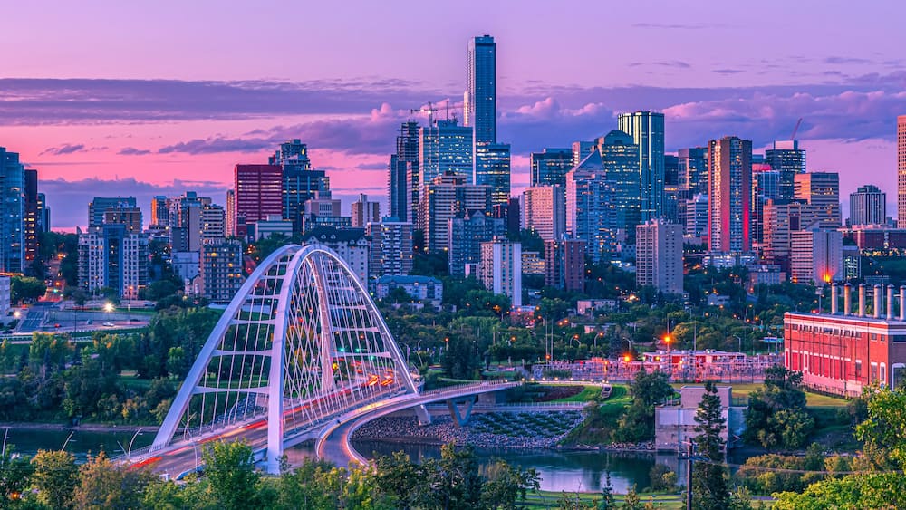 Skyline of Edmonton at dusk with a pink glow and the Walterdale Bridge crossing the North Saskatchewan River in the River Valley; Edmonton, Alberta, Canada
