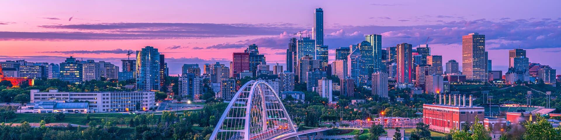 Skyline of Edmonton at dusk with a pink glow and the Walterdale Bridge crossing the North Saskatchewan River in the River Valley; Edmonton, Alberta, Canada