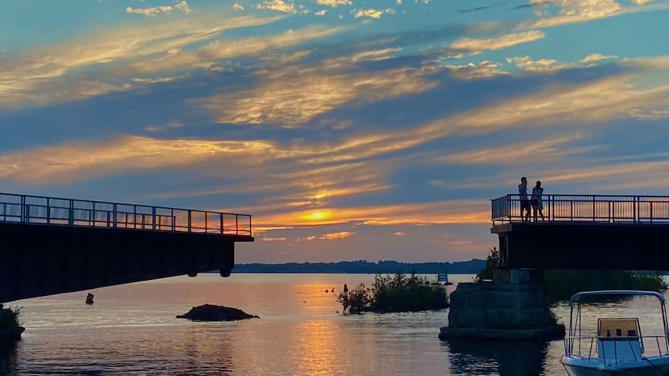 A sunset over a calm river with a bridge and a boat docked on the right.