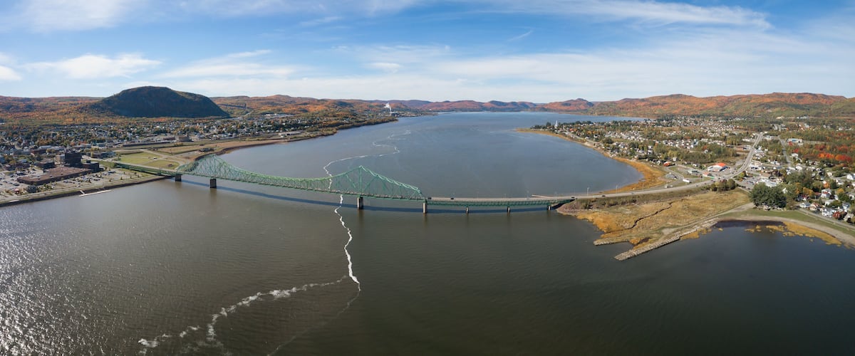 A river with a bridge, a town on the riverbank, and mountains in the background.