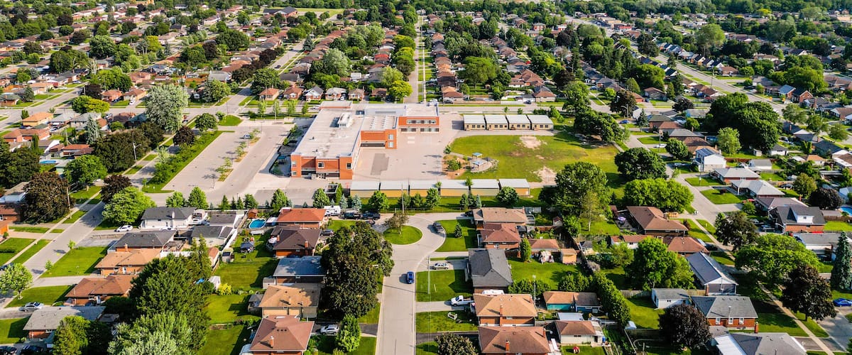 An aerial view of a suburban neighborhood with houses, green spaces, and a large building complex.