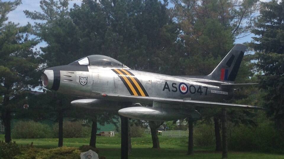 A silver fighter jet with the markings "AS 047" and "Royal Canadian Air Force" on a grassy field with trees in the background.