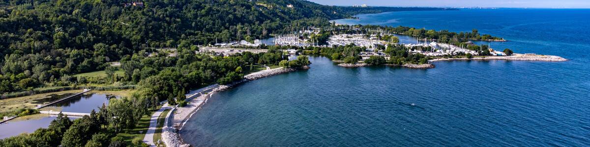 Une ville côtière dotée d’un port de plaisance, entourée de collines boisées et surplombée d’un ciel bleu azur.