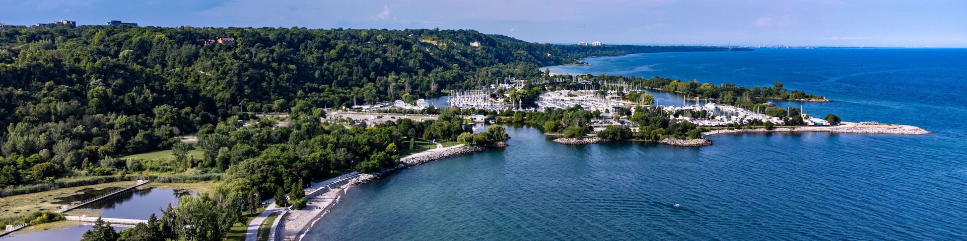Uma cidade costeira com um porto de recreio, rodeada por colinas arborizadas e um céu azul límpido.