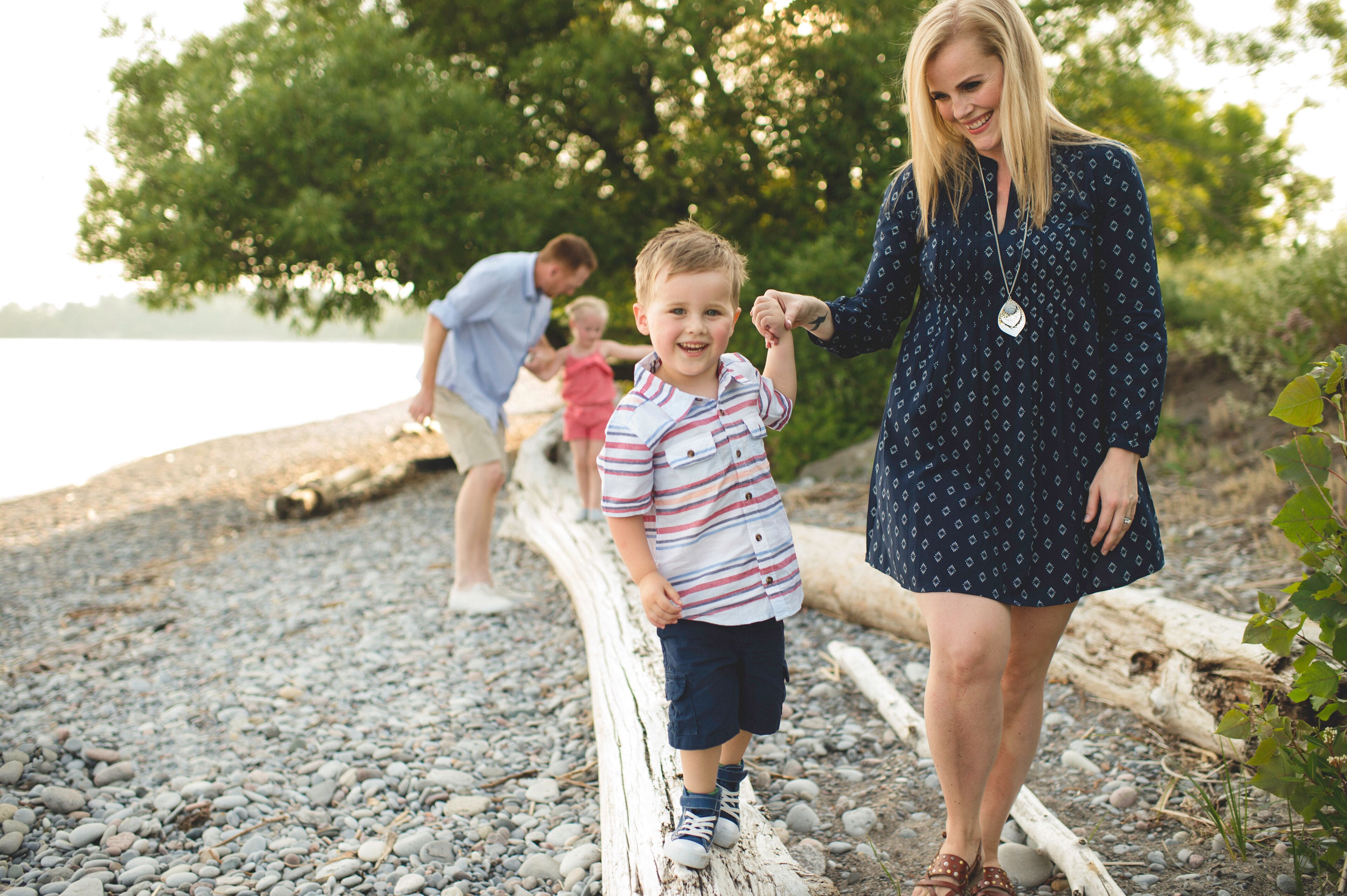 Mid adult woman holding hands with boy on tree trunk at Lake Ontario, Oshawa, Canada
