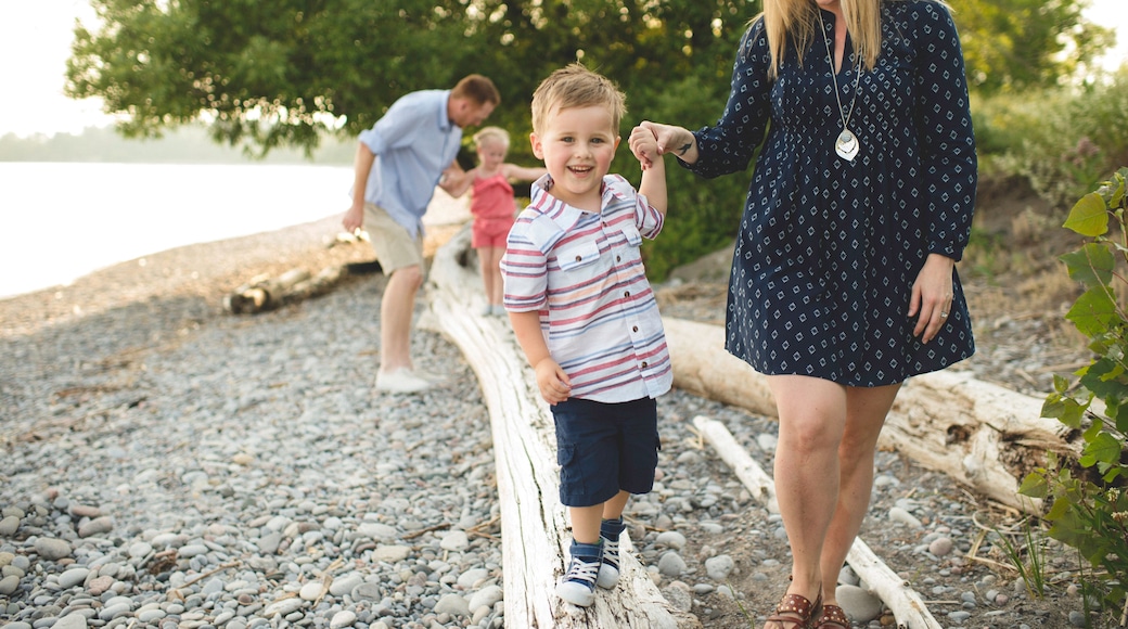 Mid adult woman holding hands with boy on tree trunk at Lake Ontario, Oshawa, Canada