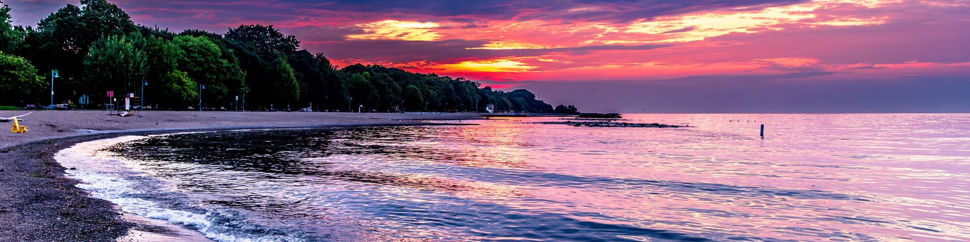 dawn over kew beach toronto with firey red orange and blue sky reflected in the water of lake ontario white foam at waters edge room for text
