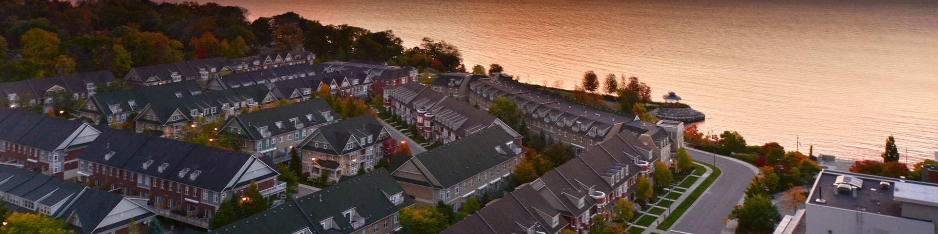 A coastal residential area with houses and a body of water during sunset.