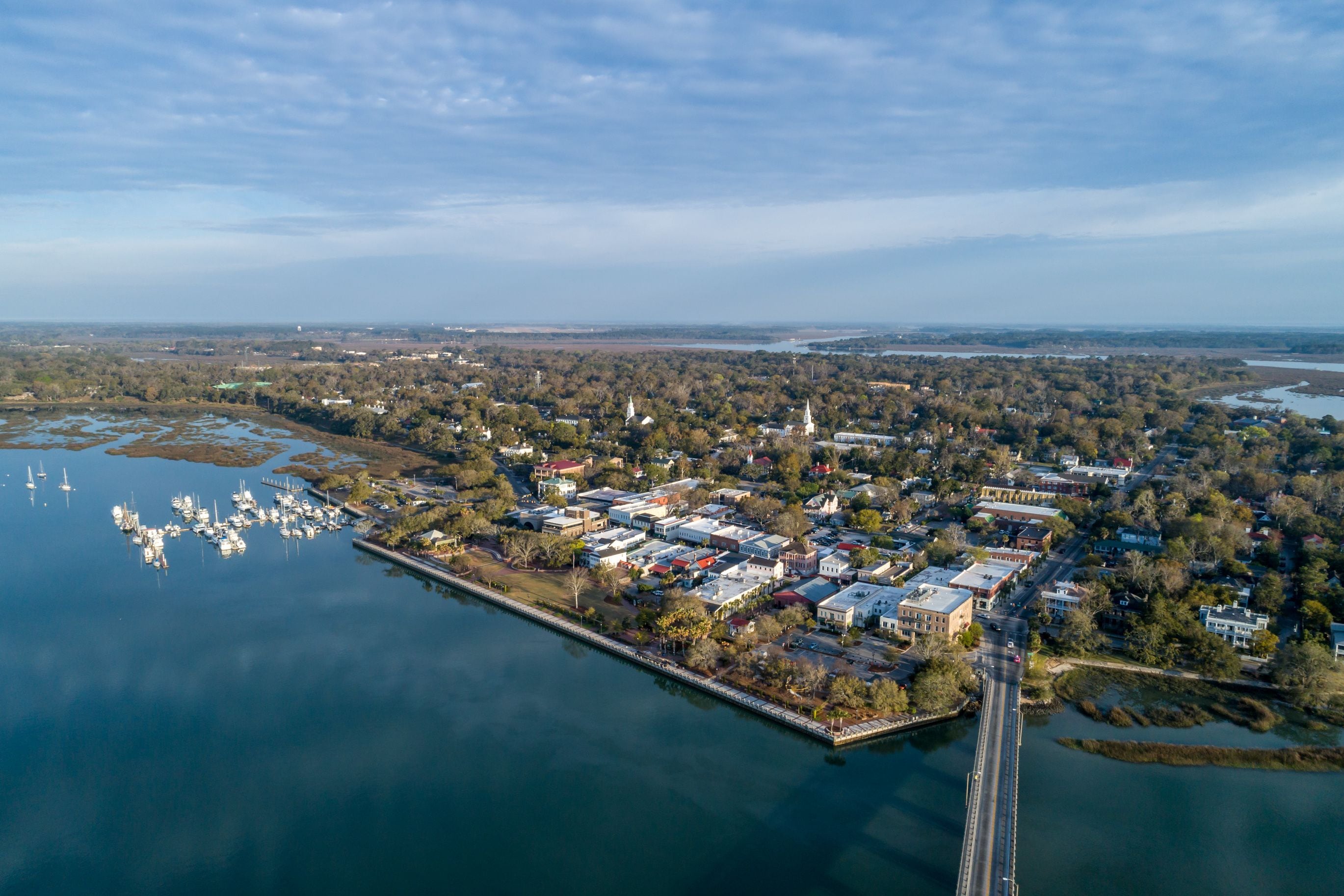 An aerial view of a coastal town with a marina, a bridge, and surrounding greenery.
