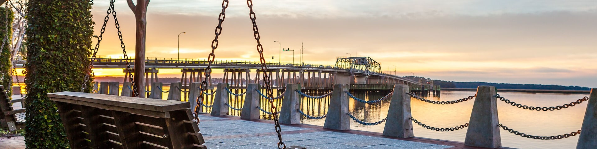 Um banco de balanço de madeira com vista para uma orla, com uma ponte ao fundo.