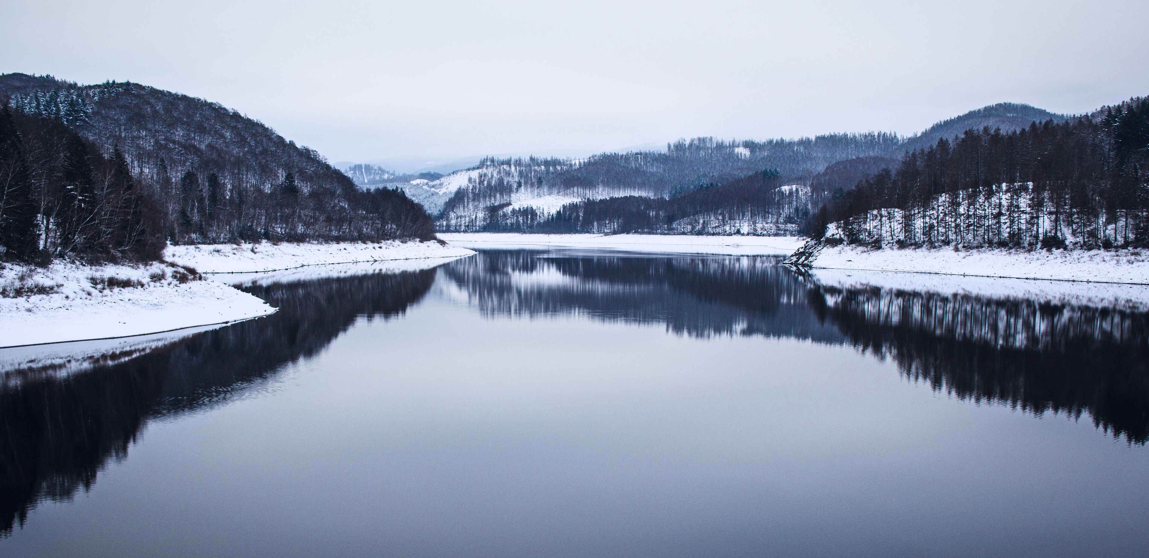 A calm river surrounded by snow-covered hills and dense forests.